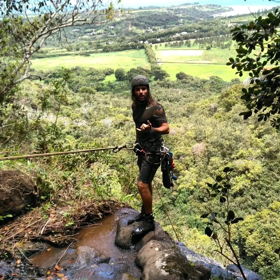 Guide on rope at a cliff edge above a green valley