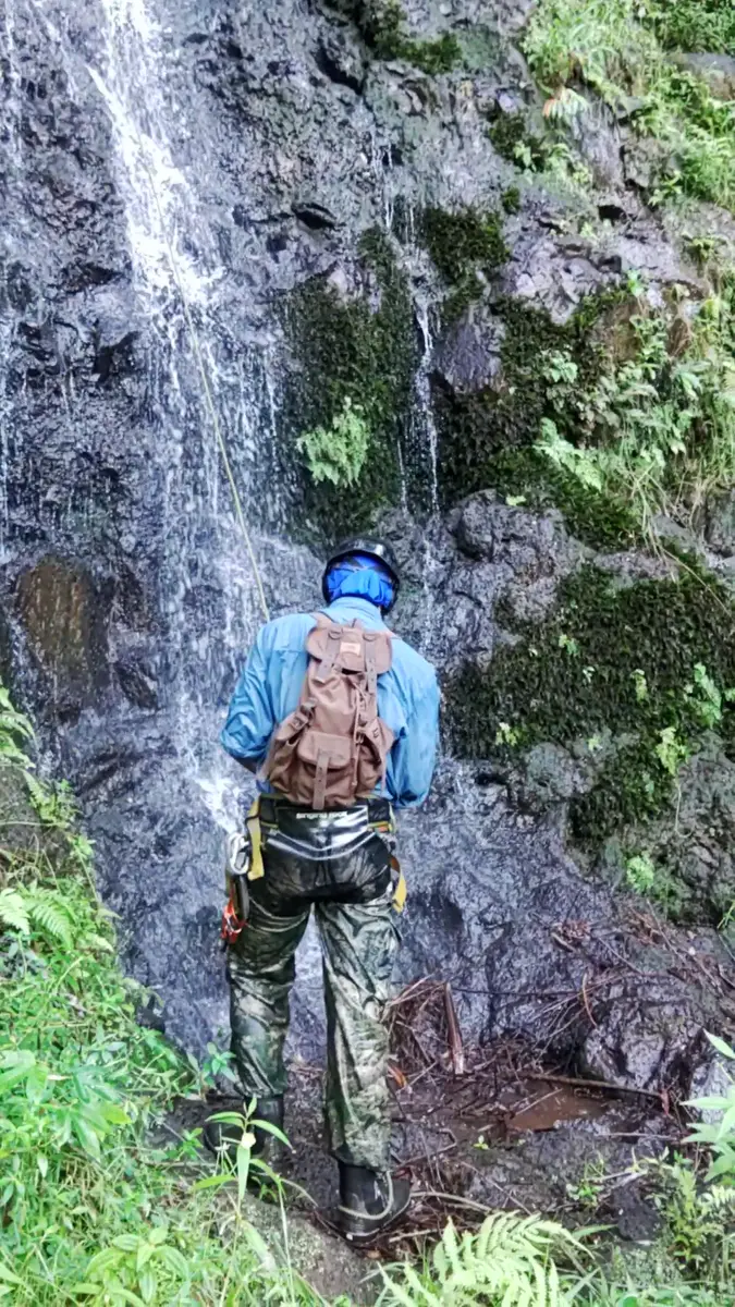 A guide from behind wearing a harness, helmet and pack at the base of a waterfall