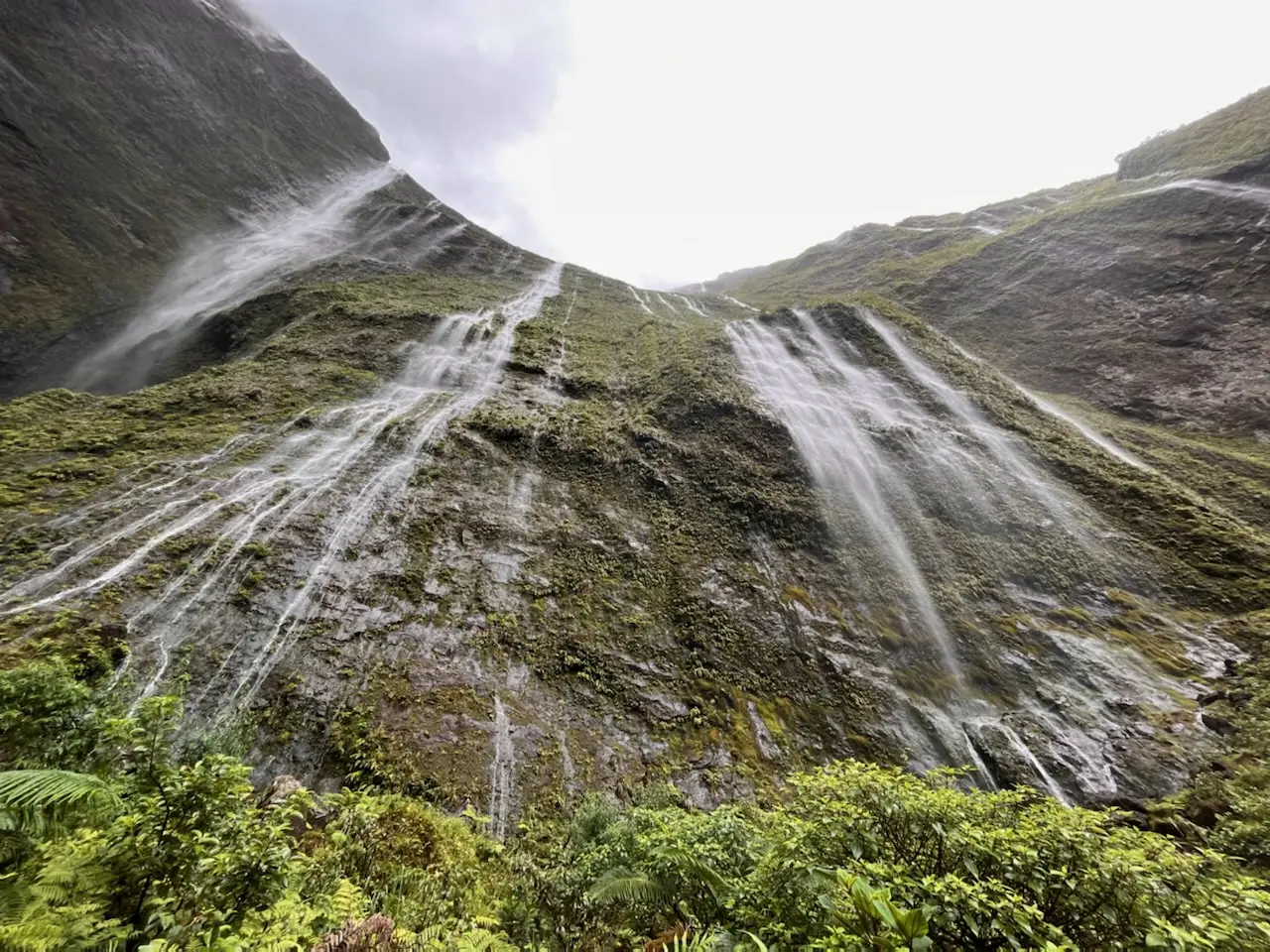 A green cliff streaked with dozens of thin waterfalls