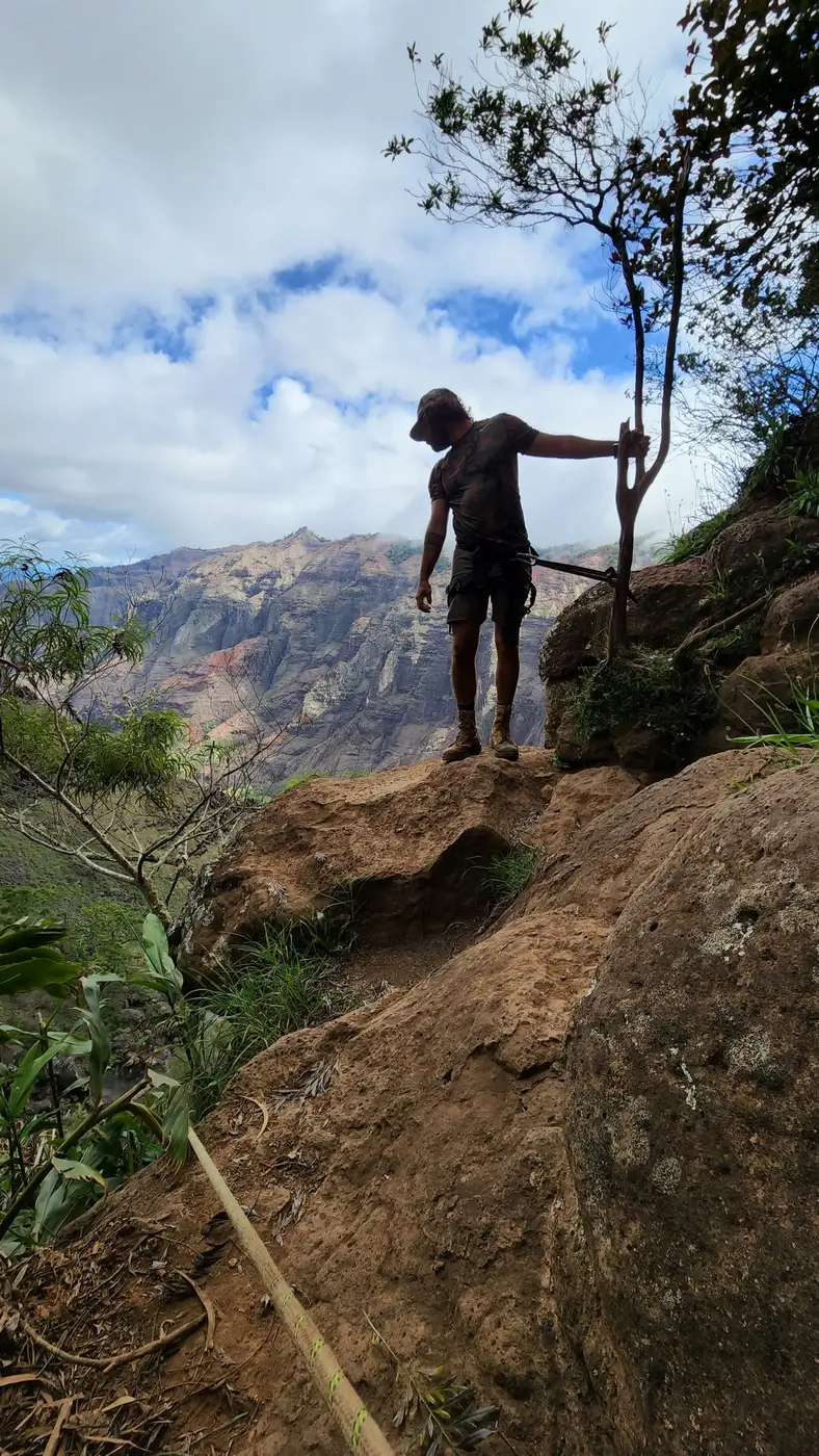 A hiker standing on a red dirt ridge above a canyon
