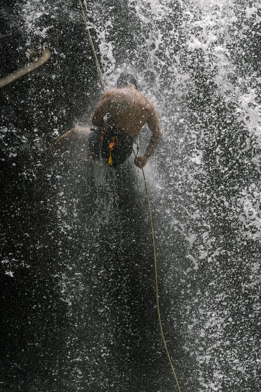 A rappeller passing through the curtain of a waterfall