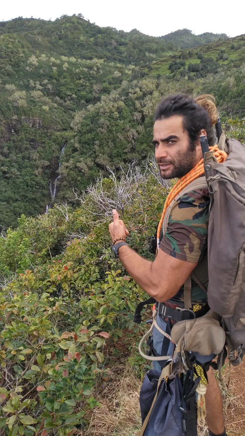 Renan Gobbet Hernandez with a coiled rope and pack on a ridge above a jungle waterfall